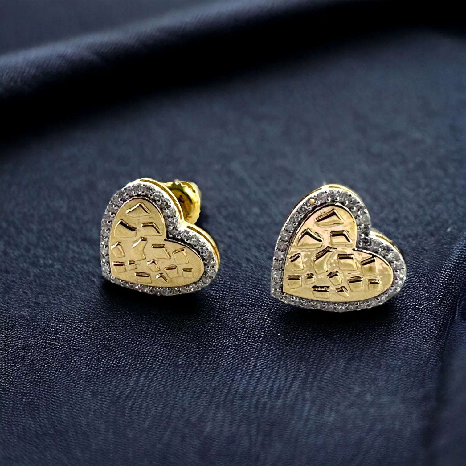 Close-up of 10KT gold 10mm heart-shaped diamond earrings with 0.15ct total SI diamonds and textured nugget center, shown on dark fabric to emphasize sparkle and halo design