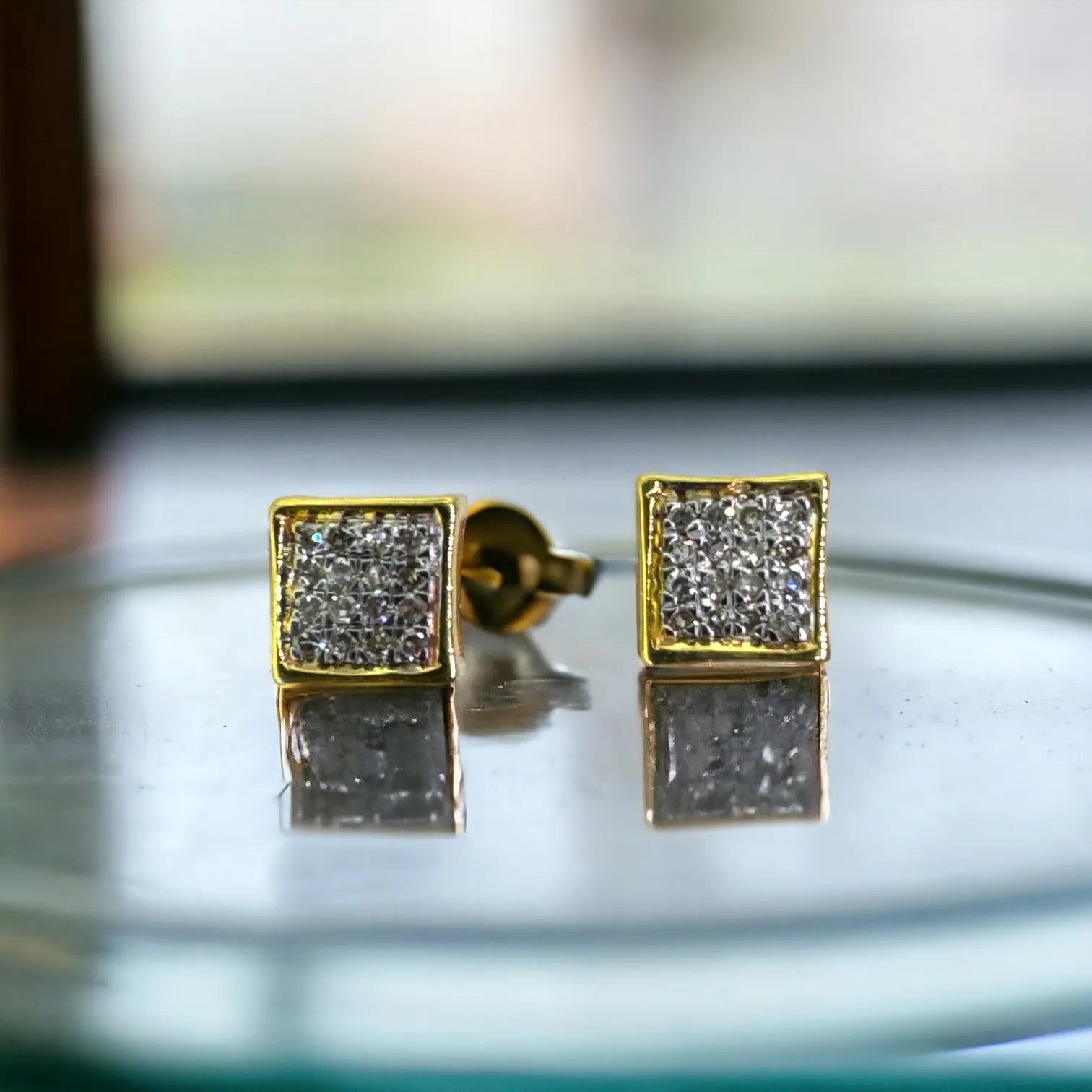 Front close-up of luxury 10KT yellow gold 5mm square pave diamond studs totaling 0.09 carats SI clarity diamonds, displayed on reflective glass surface