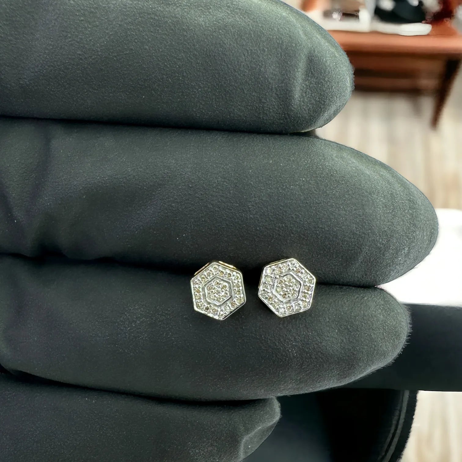 Pair of luxury 10KT yellow gold hexagon stud earrings with 0.10ct SI diamonds, displayed against dark fabric to showcase brilliance and geometric elegance