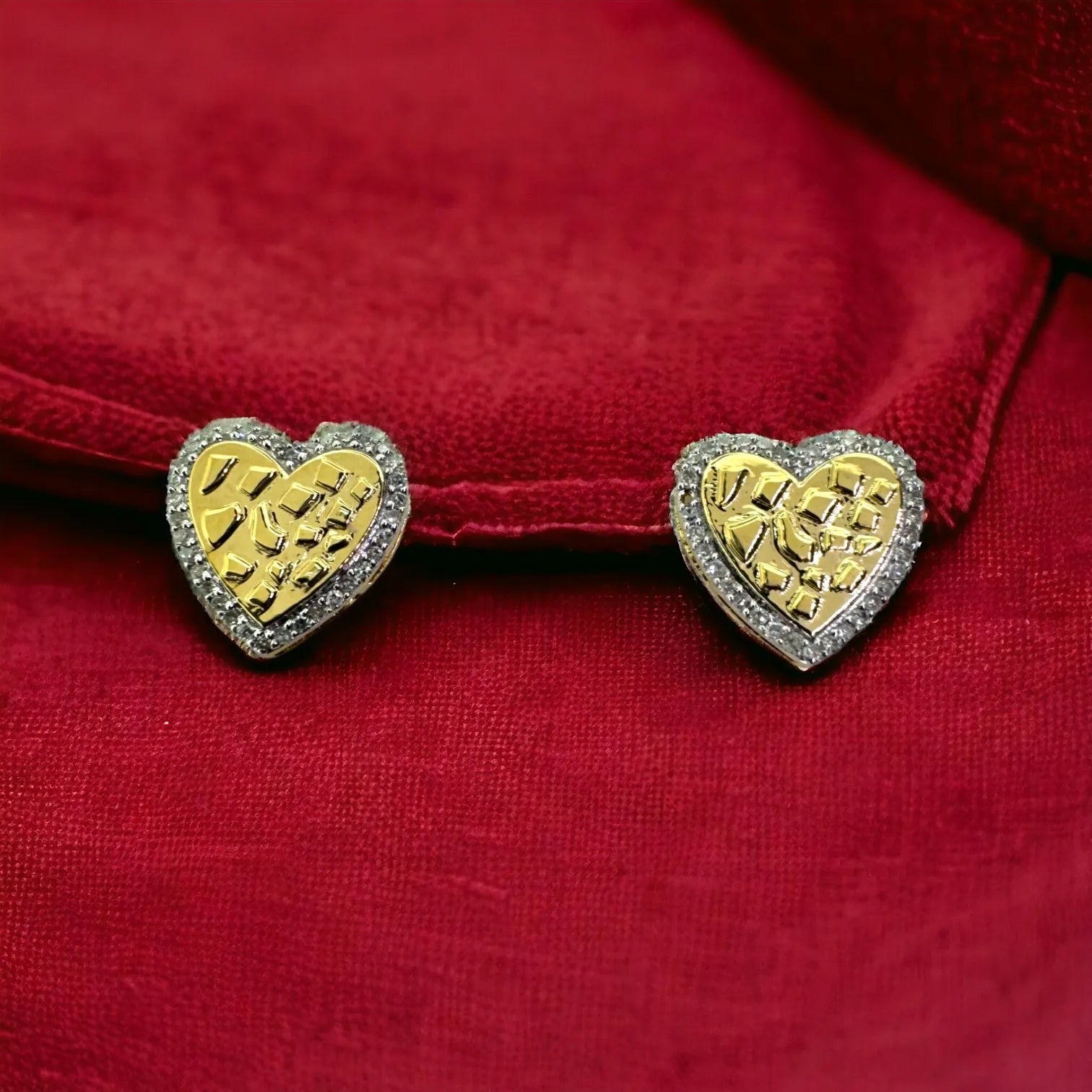 Pair of romantic 10KT yellow gold 10mm heart studs featuring textured gold nugget design surrounded by 0.15ct pave SI diamonds, displayed against rich red velvet background