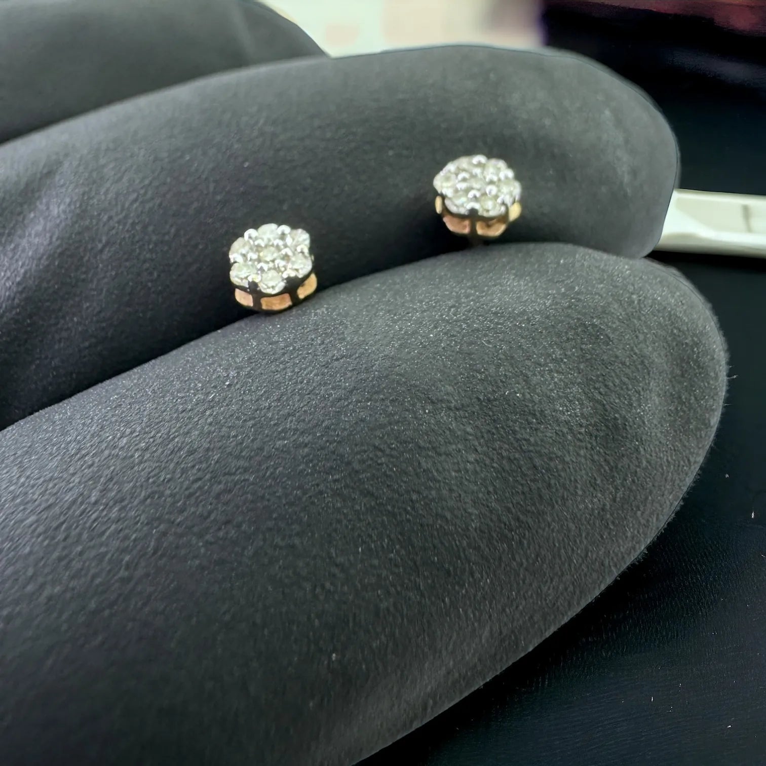 iny 10KT yellow gold flower stud earrings with 0.10 carat total SI diamonds held in gloved hand to demonstrate petite size and brilliant sparkle